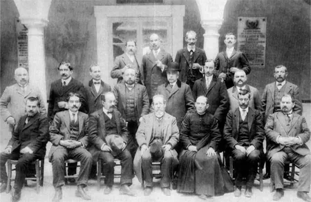 Fotografía antigua de un grupo de hombres trajeados, de pie y sentados, en un patio con columnas