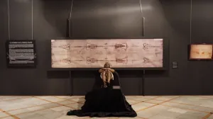 Una sala oscura con la reproducción de la Sábana Santa en la pared y una figura delante
