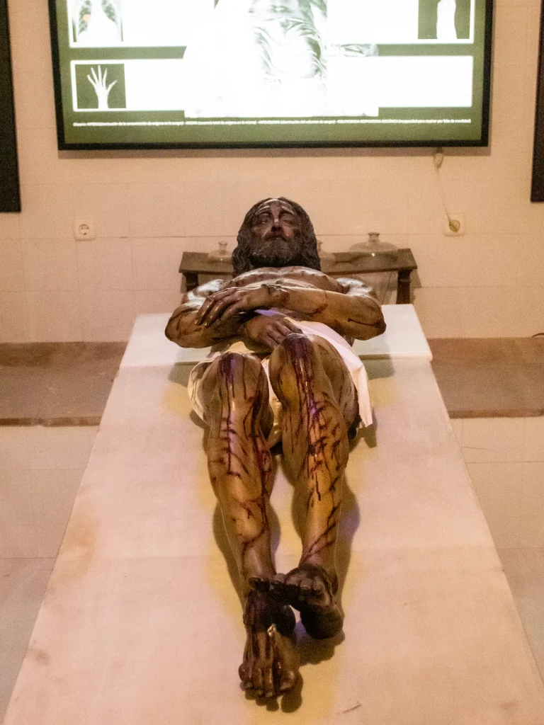 Talla del Hombre de la Sábana Santa, de Juan Manuel Miñarro: un hombre yacente, con las heridas de la Pasión, sobre una losa blanca; detrás, un panel iluminado con radiografías